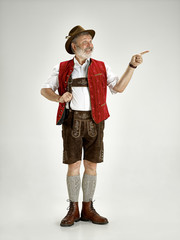 Wall Mural - Portrait of Oktoberfest senior man in hat, wearing a traditional Bavarian clothes standing at full-length at studio. The celebration, oktoberfest, festival concept