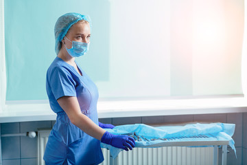 Young blond woman assistant standing near table with equipment prepating for gynecology operation. Real people models. Copy space