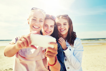 Wall Mural - summer vacation, holidays, travel, technology and people concept- group of smiling young women taking sulfide with smartphone on beach