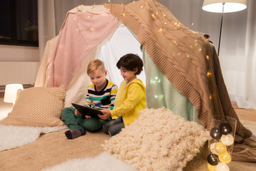 childhood, technology and hygge concept - happy little boys with tablet pc computer in kids tent at home