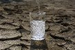 pure clear fresh water is poured into a glass beaker standing in the middle of a dry cracked clay desert land