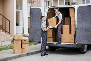 Wall Mural - Two young handsome movers wearing uniforms are unloading the van