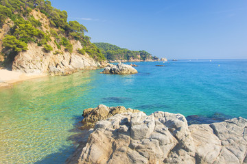 Poster - Marine tropical lagoon. Turquoise water on beach with white sand and rocks along coastline. Beaches of Lloret de Mar, Costa Brava, Spain. Clear summer day at sea. Nature of Mediterranean.
