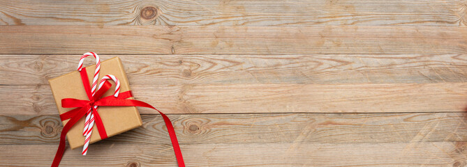 A gift box with red ribbon and candy canes on wooden background, banner, copy space, top view