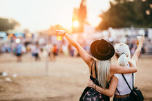 Two Female Friends Drinking Beer And Having Fun At Music Festival. Back View