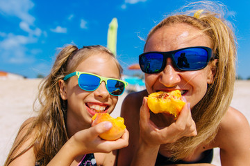 Mom and daughters eat peaches on the beach by the sea