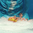 Boy having fun on the water slide in the aqua fun park. Happy falling into water and water splashes are all over.