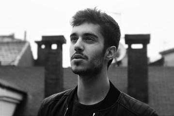 Black and white close portrait of a young light bearded spanish man on the roofs of a city