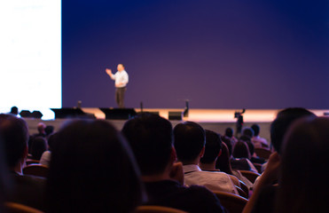 Fototapete - Presenter Presenting on Stage at Conference Hall Exhibition. Professional Lecture. Hand Up To Screen. Blurred De-focused Unidentifiable Presenter and Audience. Executive Speaker.