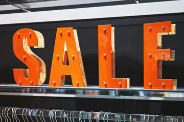 Sticker - The big bright letters SALE in the big boutique clothing store. Large sale of clothes in a large modern shopping center, mall. Rack with shoulders for clothes. Basic background for design