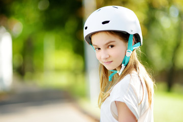 Wall Mural - Pretty little girl learning to roller skate on summer day in a park. Child wearing safety helmet enjoying roller skating ride outdoors.