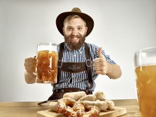 Germany, Bavaria, Upper Bavaria. The young smiling man with beer dressed in traditional Austrian or Bavarian costume in hat holding mug of beer at studio