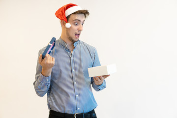 Wall Mural - Amazed Christmas guy shocked with present. Young man with wide eyes and open mouth opening present box and looking inside. Xmas surprise concept