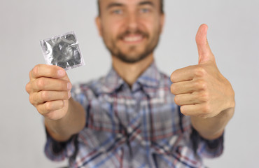 man in plaid shirt holds a new condom in hand, make gesture thumb up, joy and anticipation of pleasure