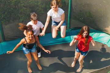 Wall Mural - Four happy friends bouncing on outdoor trampoline