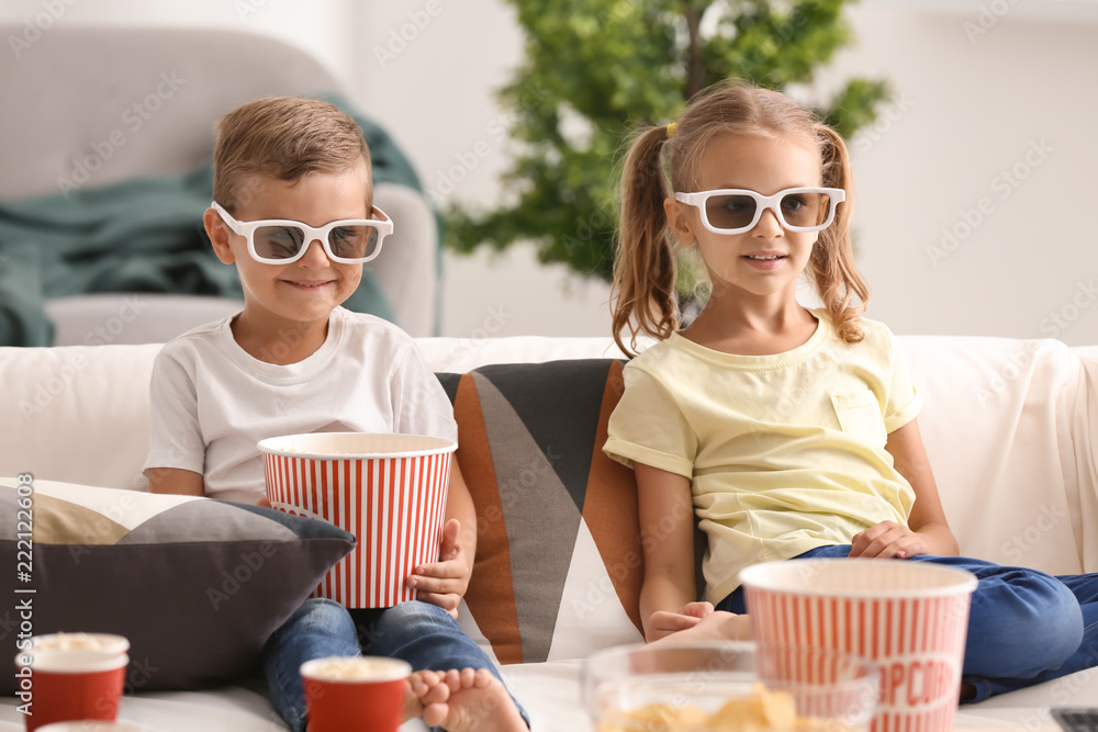 Cute children eating popcorn while watching TV at home