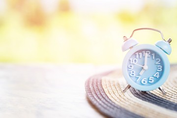 Wall Mural - small sized old vintage retro alarm clock blue with bells Put on a Woman beach hat . colorful hat , on wooden background wallpaper. atmosphere Morning sunshine. 