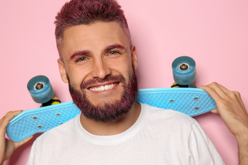 Poster - Portrait of handsome man with dyed hair and beard holding skateboard on color background