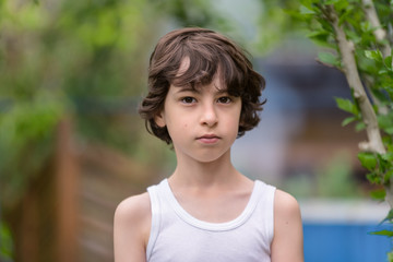 Portrait of a boy in a sleeveless shirt on a nature background. Country style.