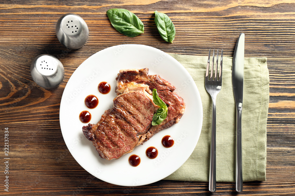 Plate with delicious grilled steak and sauce on wooden table