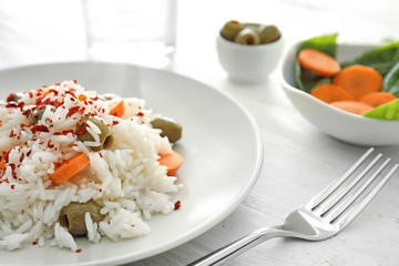 Plate with tasty boiled rice and vegetables on white wooden table, closeup