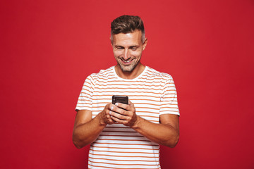 Sticker - Image of caucasian man in striped t-shirt smiling and holding mobile phone, isolated over red background