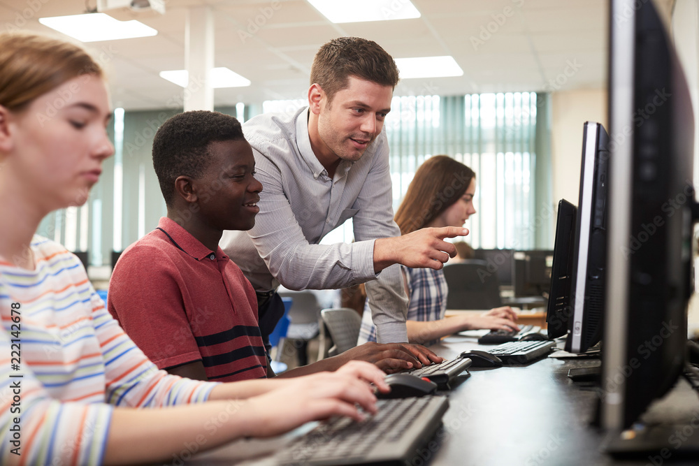 Teacher Helping Male High School Student Working In Computer Class ...
