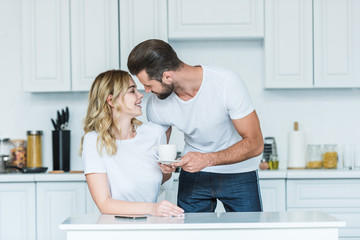 Wall Mural - happy young couple holding cup of coffee and smiling each other at morning