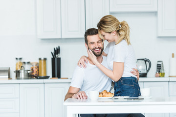 Wall Mural - attractive smiling girl hugging happy boyfriend while having breakfast together