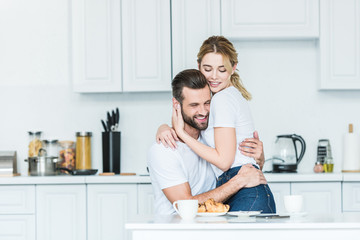 Wall Mural - beautiful happy young couple in love hugging during breakfast in kitchen