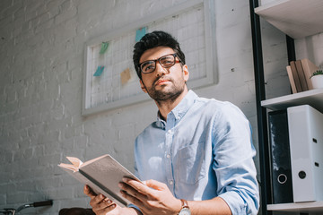 Wall Mural - handsome architect in glasses holding book and looking away in office