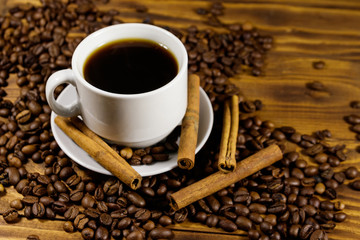 Cup of coffee, roasted coffee beans and cinnamon sticks on wooden table