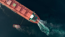 Aerial Shot Of A Cargo Ship Approaching Port With Help Of Towing Ship