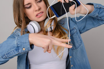 Concept of wireless headphones. Annoyed woman wants to cut the cord/wire to the headphones, she is making scissors with her fingers.