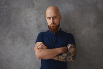 Angry dad staring at nasty children, frowning and crossing arms. Bearded macho man with furious displeased expression posing in studio with arms folded, demonstrating hostility and disrespect