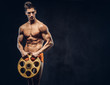 © Fxquadro - Handsome naked ectomorph bodybuilder with stylish hair in underpants posing with a barbell disk on a dark background.