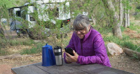 Wall Mural - Active senior woman resting on park bench texting on smart phone in nature