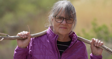 Wall Mural - Tight shot of serious elderly lady out in nature holding dead tree branch