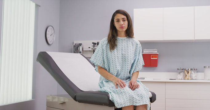 Wall Mural -  - Close up of lovely latina woman seated on medical reclined chair in hospital clinic. Portrait of attractive mixed ethnic patient looking at camera from inside medical clinic wearing somber expression