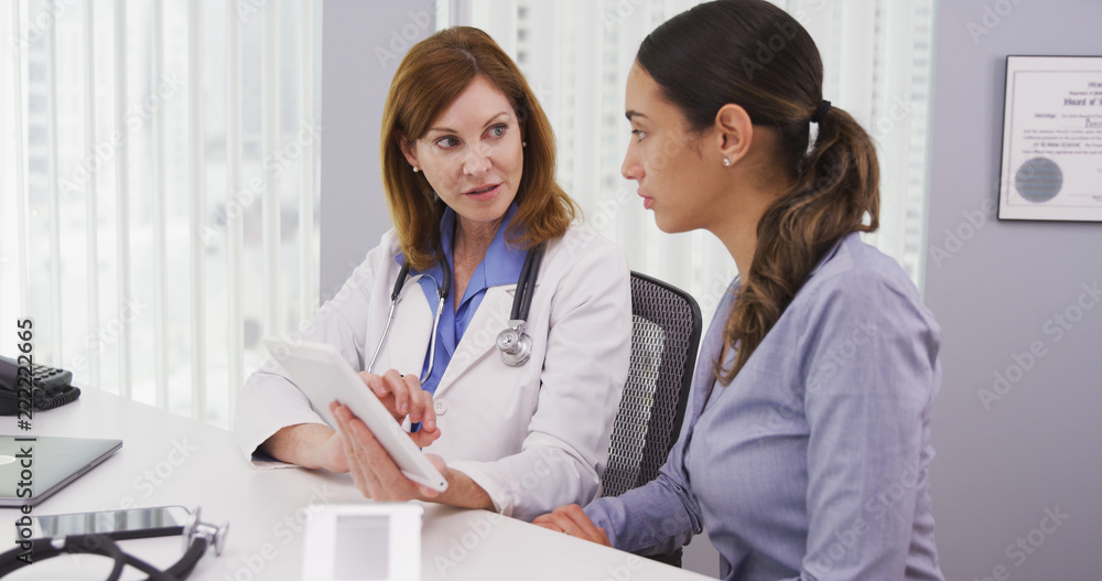 Senior medical physician using tablet computer to share results of patients health condition. Mid aged doctor and young patient looking at high tech tablet indoors medical clinic