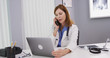 © Mark Adams - Attractive mid aged doctor using latop computer while talking on smartphone with colleague. Charming senior physician sitting in her office looking at notebook computer and chatting on cell phone