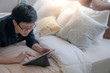 © zephyr_p - Young Asian business man using digital tablet and pen while lying on bed in cozy bedroom. Home living lifestyle with modern electronic gadget concept