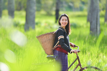 Wall Mural - Traditional Hmong girl with basket of agricultural crops walking with bicycles in forest Happy Hmong girl smiling with green nature in Sapa city, northern Vietnam