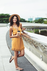 Wall Mural - Happy attractive Asian woman standing on bridge and drinking take-out coffee