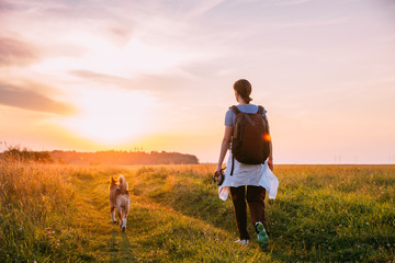 Young Woman Backpacker Walking With Dog In Summer Meadow Grass D