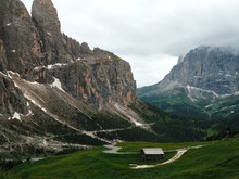 A Picturesque Panorama Of The Dolomites. There Are Huge Mountains Covered With Snow, Coniferous Forests And A Lonely House Hut Used As A Point Of Pass For Climbers