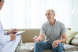© DragonImages - Elderly man sitting on sofa and sharing complaints with doctor during home visit