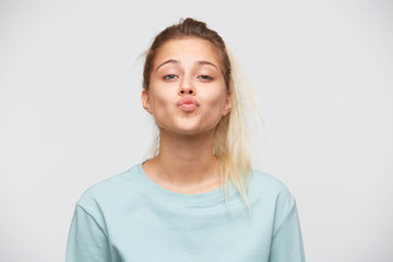 Wall Mural - Closeup of playful attractive young woman with blonde hair and ponytail wears blue sweatshirt flirting and kissing isolated over white background