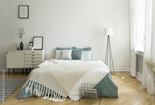 Fotografía A big comfortable bed with pale sage green and white linen, pillows and blanket in a woman's bright bedroom interior with windows