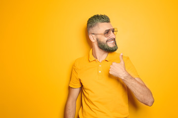 Poster - Portrait of handsome man with dyed hair and beard showing thumb-up gesture on color background